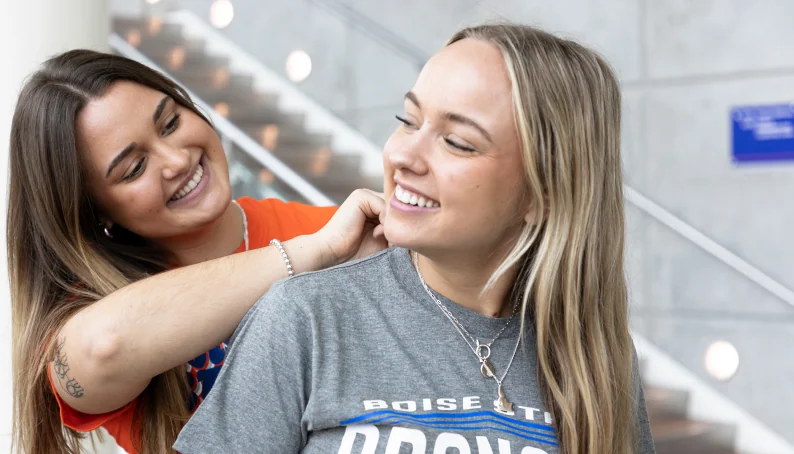 One person putting a necklace on another inside the Bronco Shop.