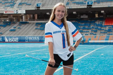 Student in a white Boise State jersey standing on the blue turf for Game Day.
