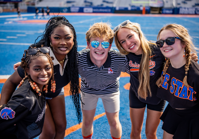 Slideshow image showing a 5 students on the blue in black gear for Gear Up Monday. Dark mode game this Saturday!
